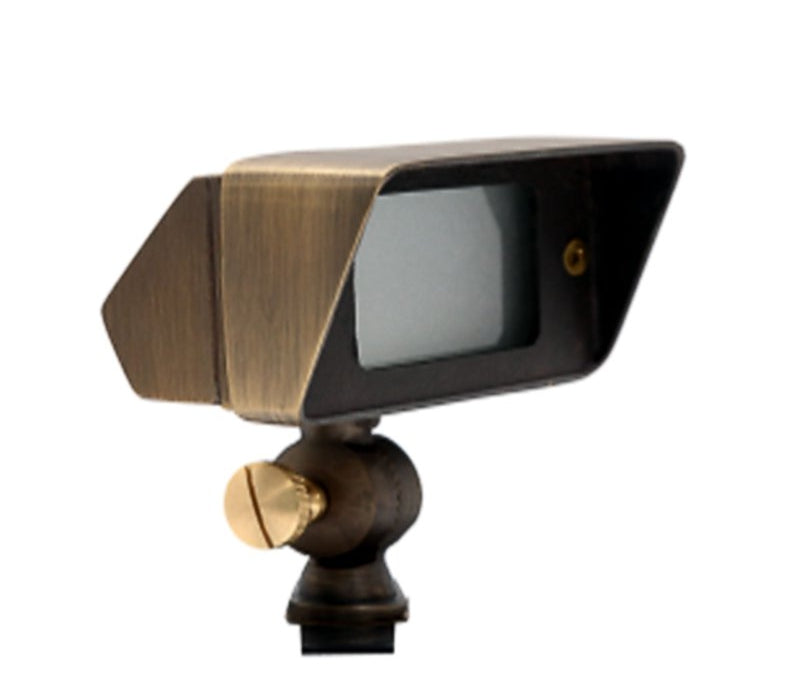 An antique brass wall washer wide accent light with a transparent glass lens and a brass fixture mounted on a ground stake.