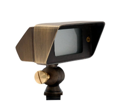 An antique brass wall washer wide accent light with a transparent glass lens and a brass fixture mounted on a ground stake.